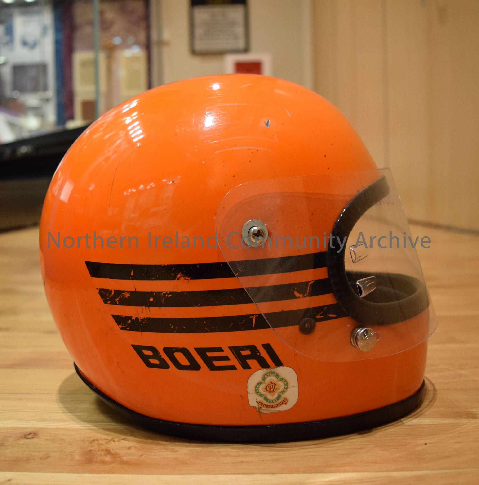 Boeri motorcycle helmet belonging to Joey Dunlop. Orange with a single black running over the top and three black stripes on either side. – 2016.107 (5)