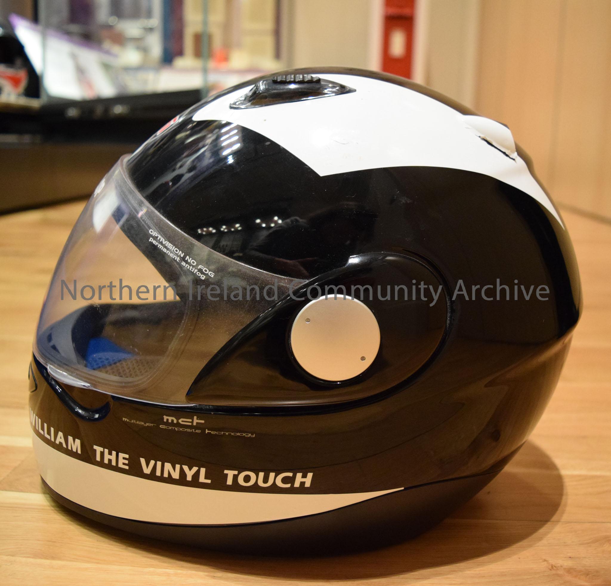 Arashi motorcycle helmet belonging to William Dunlop. Black with white stripe down the middle and two white triangular segments down each side. – 2016.112 (3)