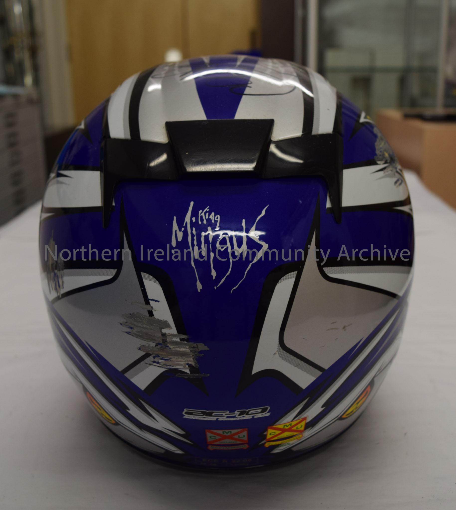 HJC motorcycle helmet belonging to Caroline Cells. Dark blue helmet with orange pattern on both sides and black, white and silver pattern across the t… – 2016.36 (4)