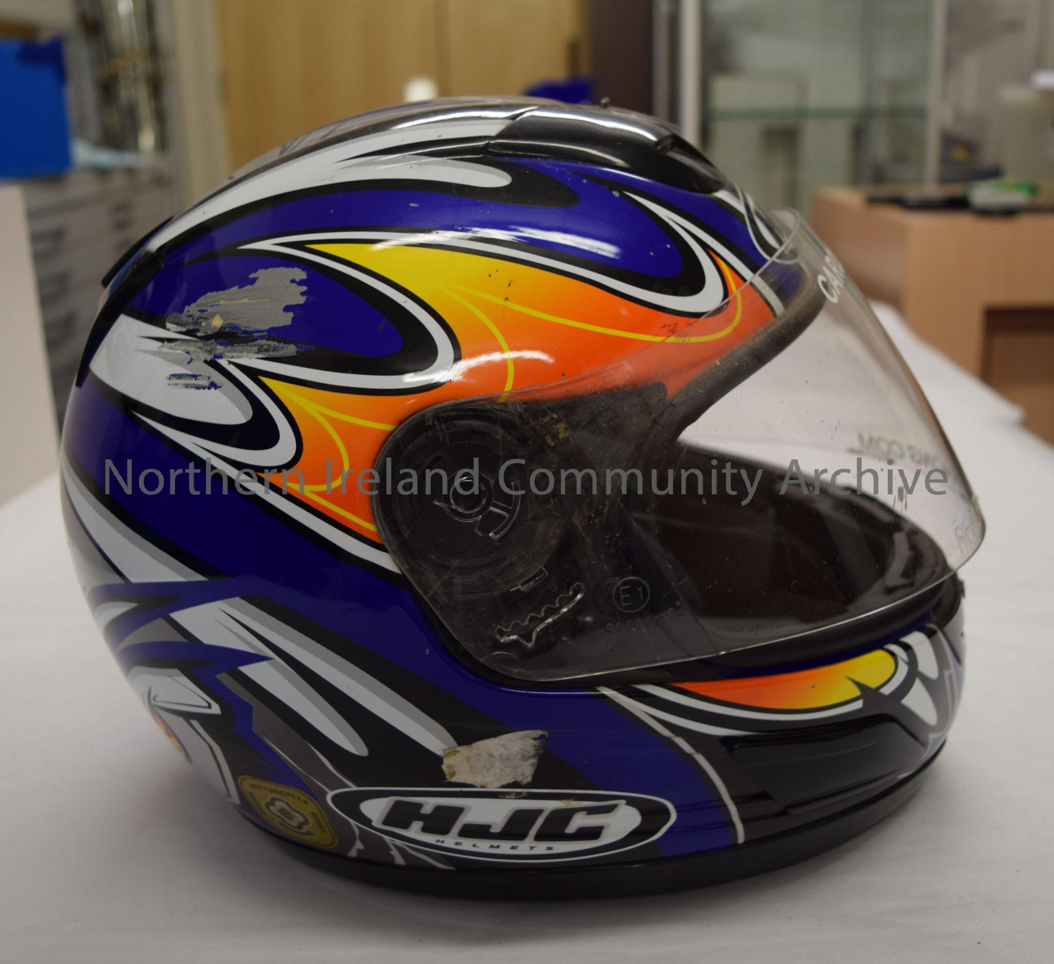 HJC motorcycle helmet belonging to Caroline Cells. Dark blue helmet with orange pattern on both sides and black, white and silver pattern across the t… – 2016.36 (5)