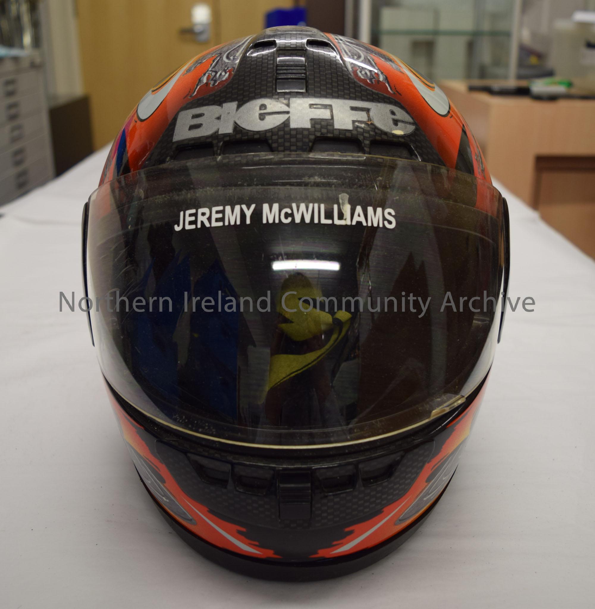 Bieffe motorcycle helmet belonging to Jeremy McWilliams. Black helmet with an orange and grey pattern on it. Small Light and dark grey checked pattern… – 2016.42 (2)