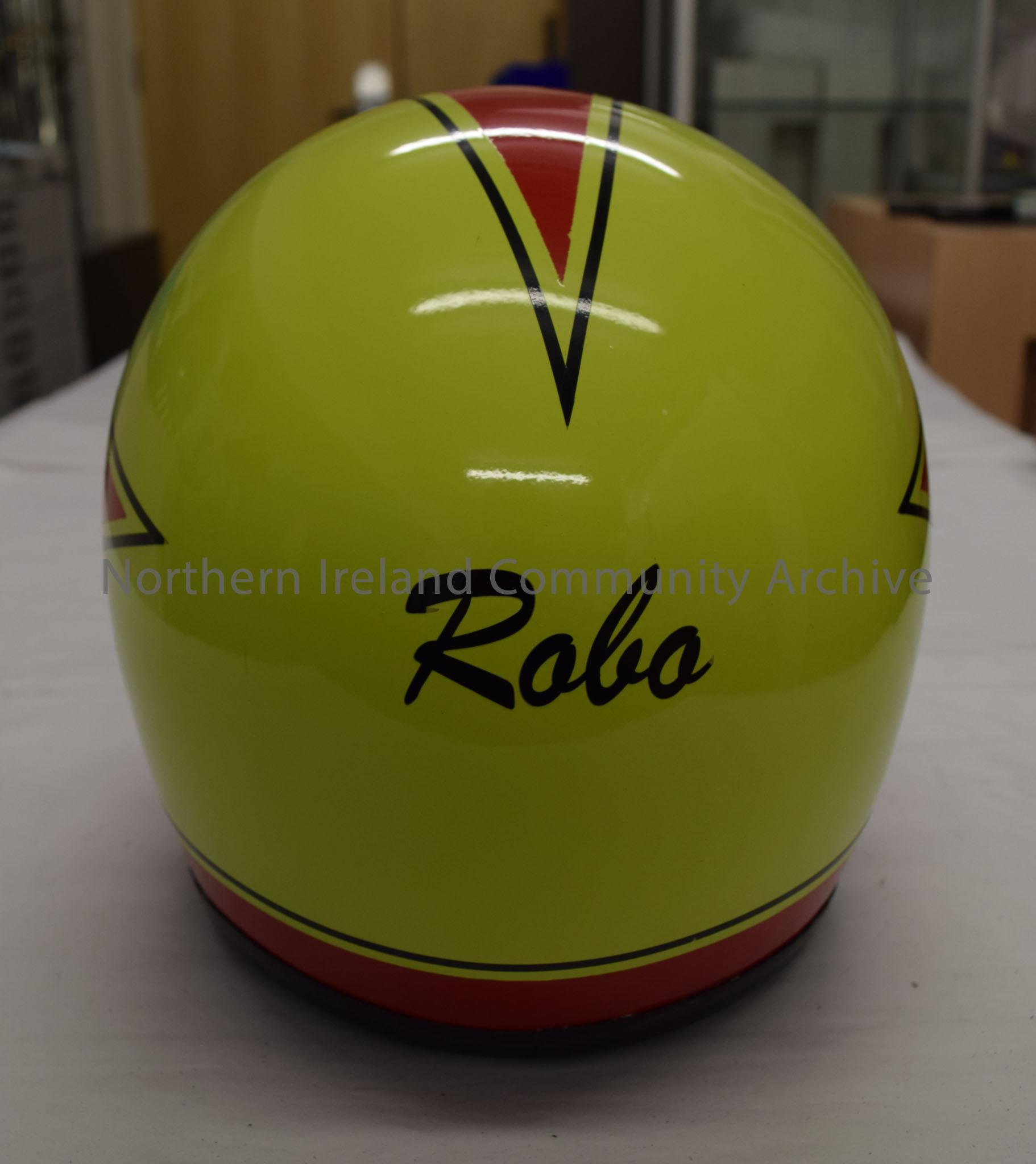 Motorcycle helmet belonging to Mervyn Robinson. Red at the front reaching back to three points with a green/yellow background and a black border. Silh… – 2016.52 (4)