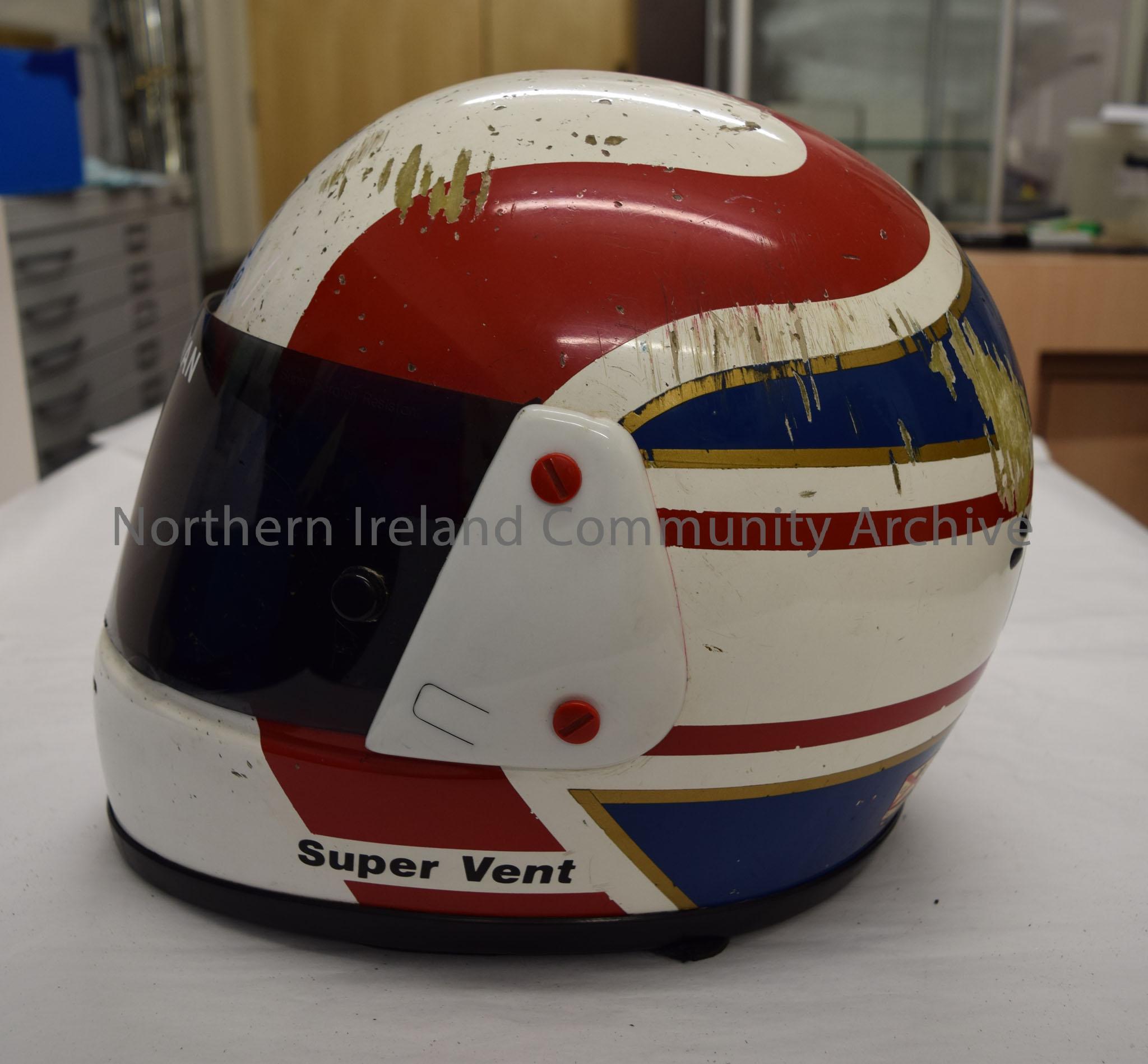 Arai motorcycle helmet belonging to Addie Swan. White helmet with red “m” shaped pattern on top a blue band with gold border around the back and botto… – 2016.56 (3)