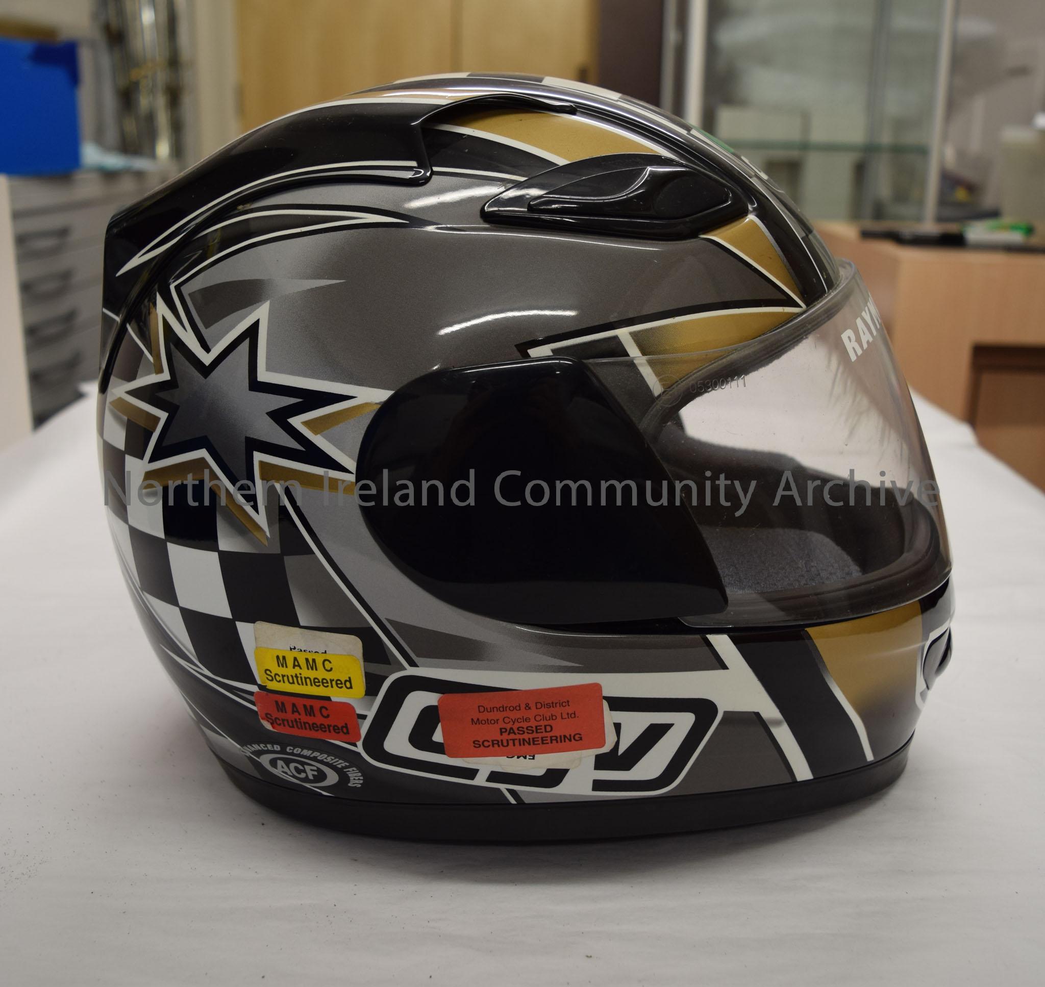 AGV motorcycle helmet belonging to Raymond Hodge. Black helmet with dark grey and gold pattern. Black and white chequered pattern down the middle. – 2016.77 (5)