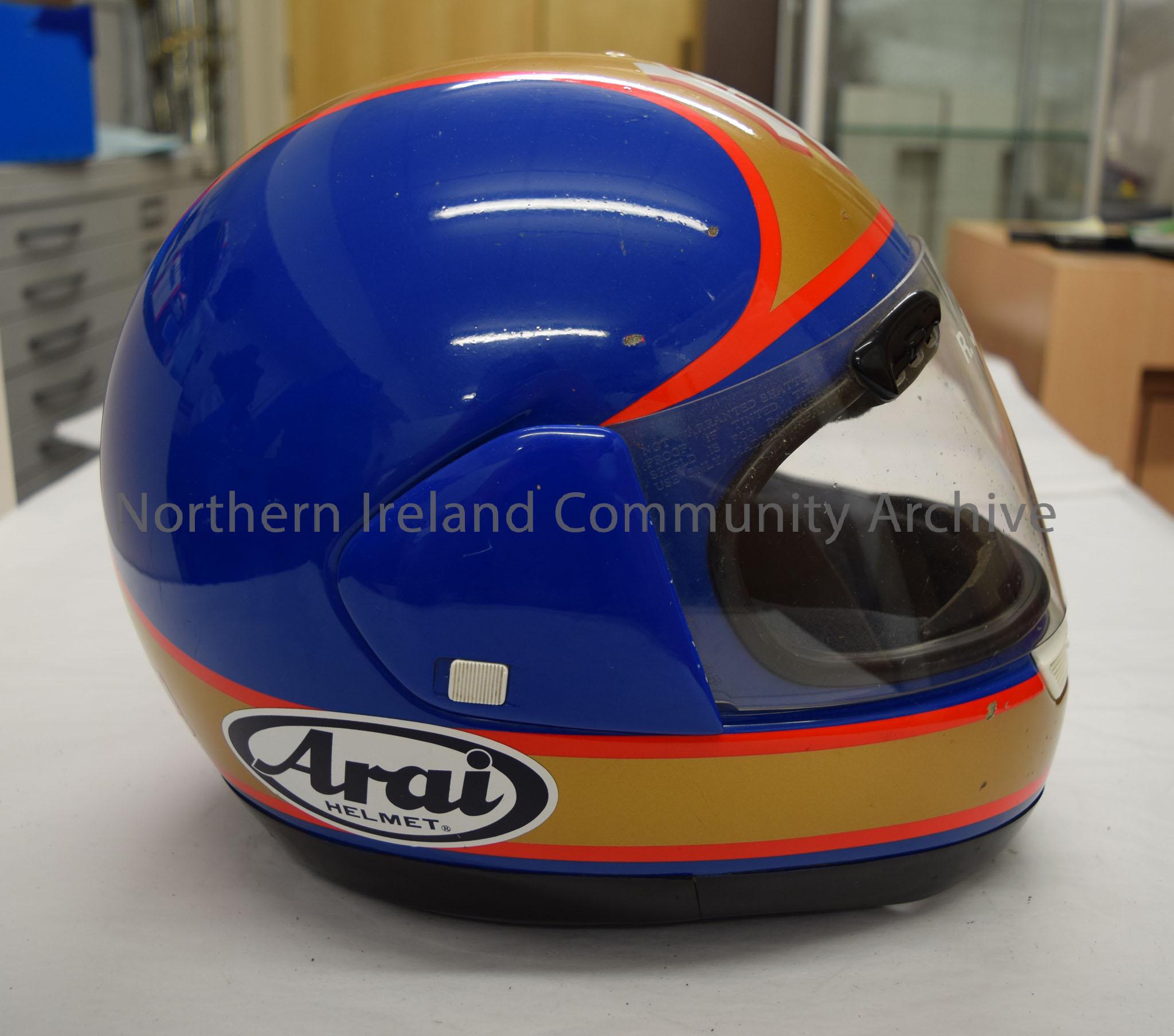 Arai motorcycle helmet belonging to R. J. Hazleton. Blue helmet with a gold stripe that runs down the middle and around the bottom with a red trim. R … – 2016.93 (5)