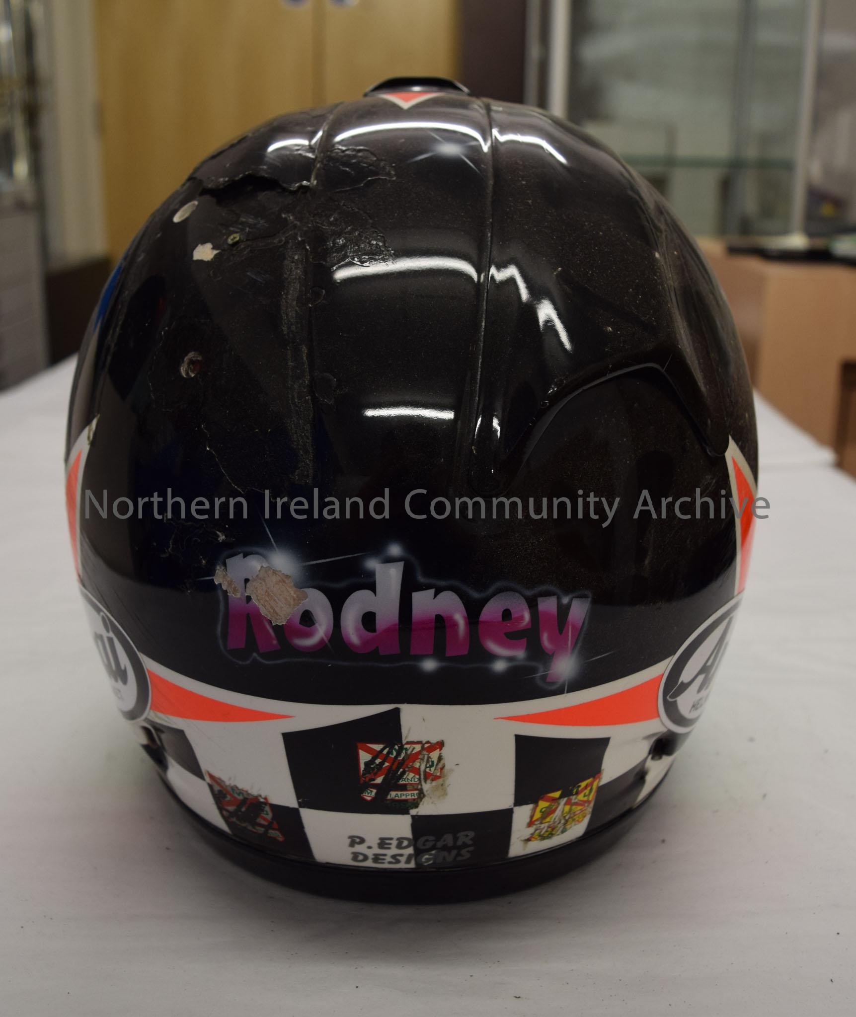 Arai motorcycle helmet belonging to Rodney McCurdy. Black helmet with top of a star in orange at the front and two bright orange stars on the side. Ch… – 2016.97 (4)