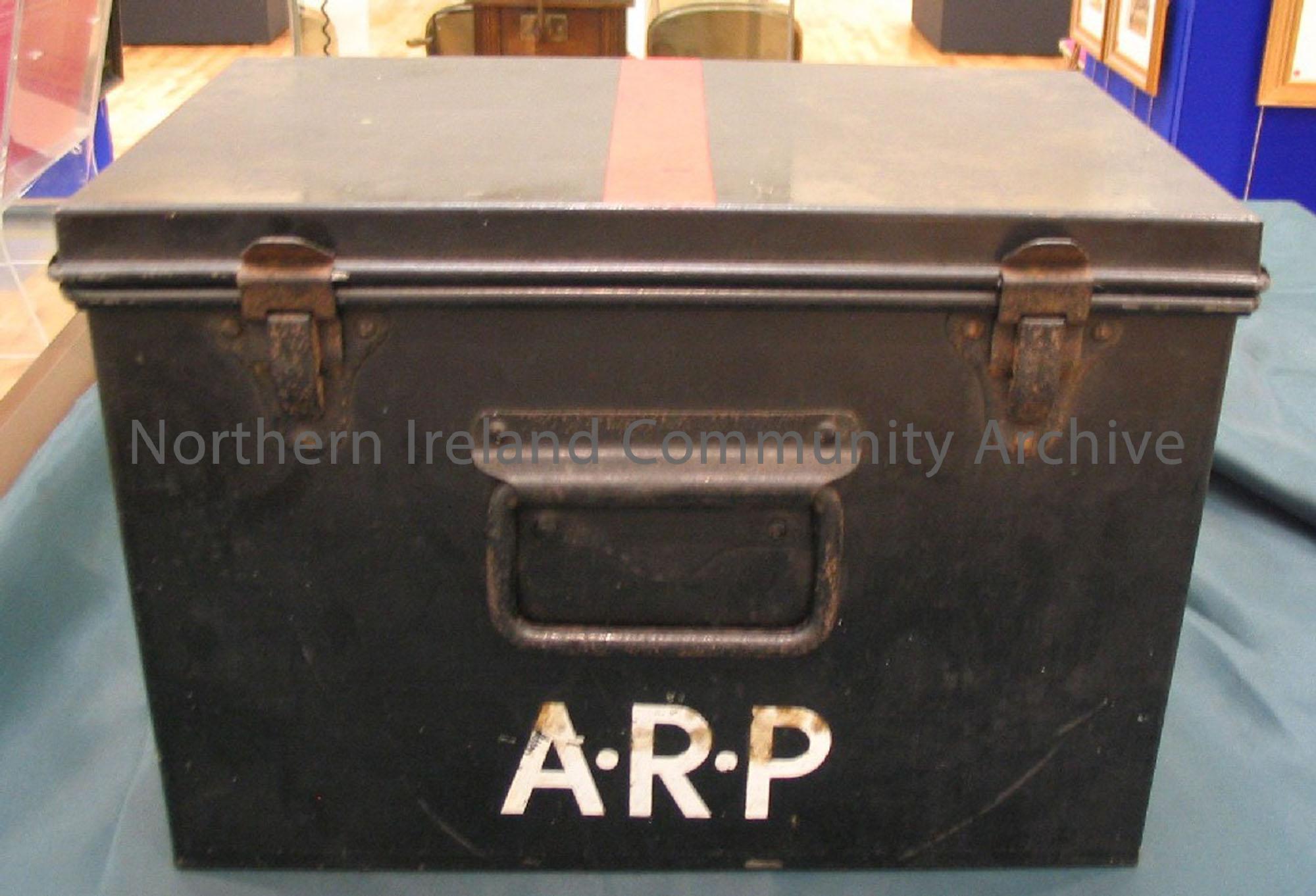 Air raid precaution equipment box. Box with hinged lid on top, coloured black with a red stripe on the lid and ARP written on side.