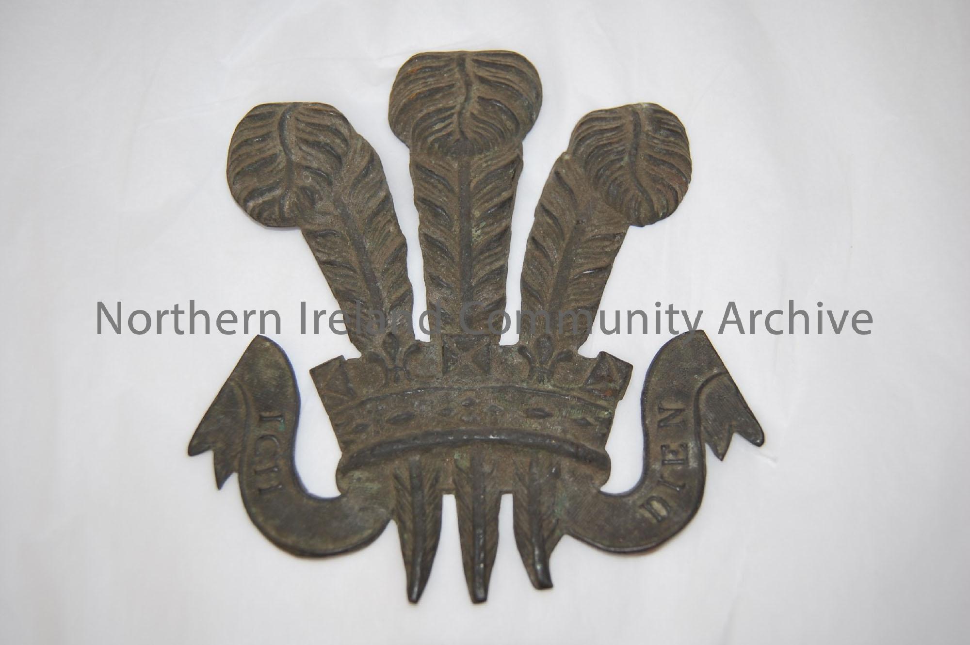 Possibly a military crest, three feathers coming out of a crown over a scroll with “Ich Dien” motto.