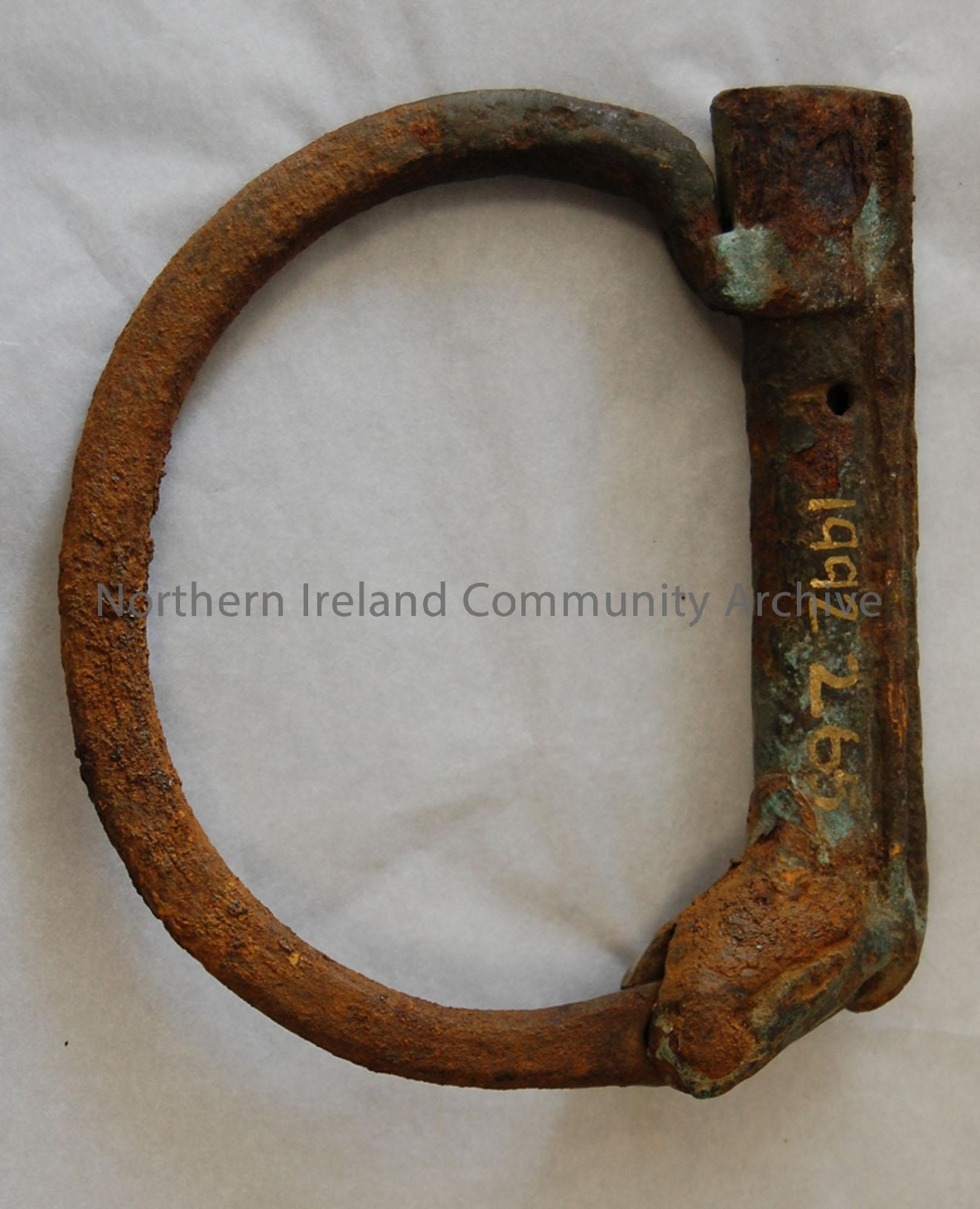 Object is shaped like a single ankle or hand cuff; the cuff is locked with a pin of wood; severe surface corrosion