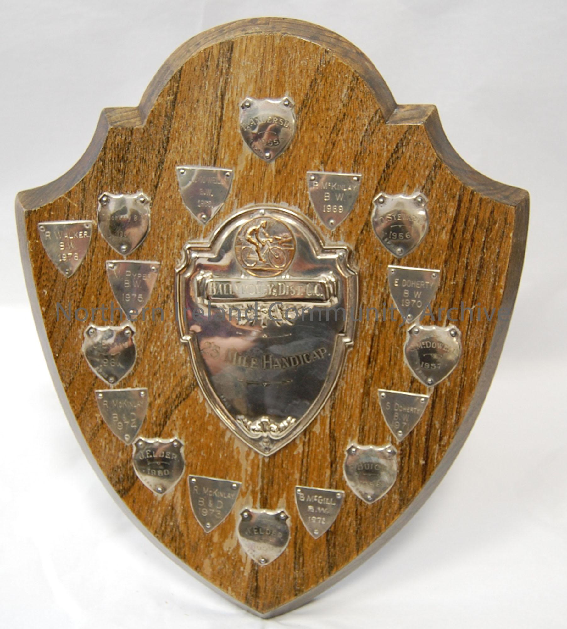 Wooden shield with smaller metal plaques naming winners of shield 1955-1976. Central shield engraved ’25 mile Handicap’. Stand attached to the back ma…