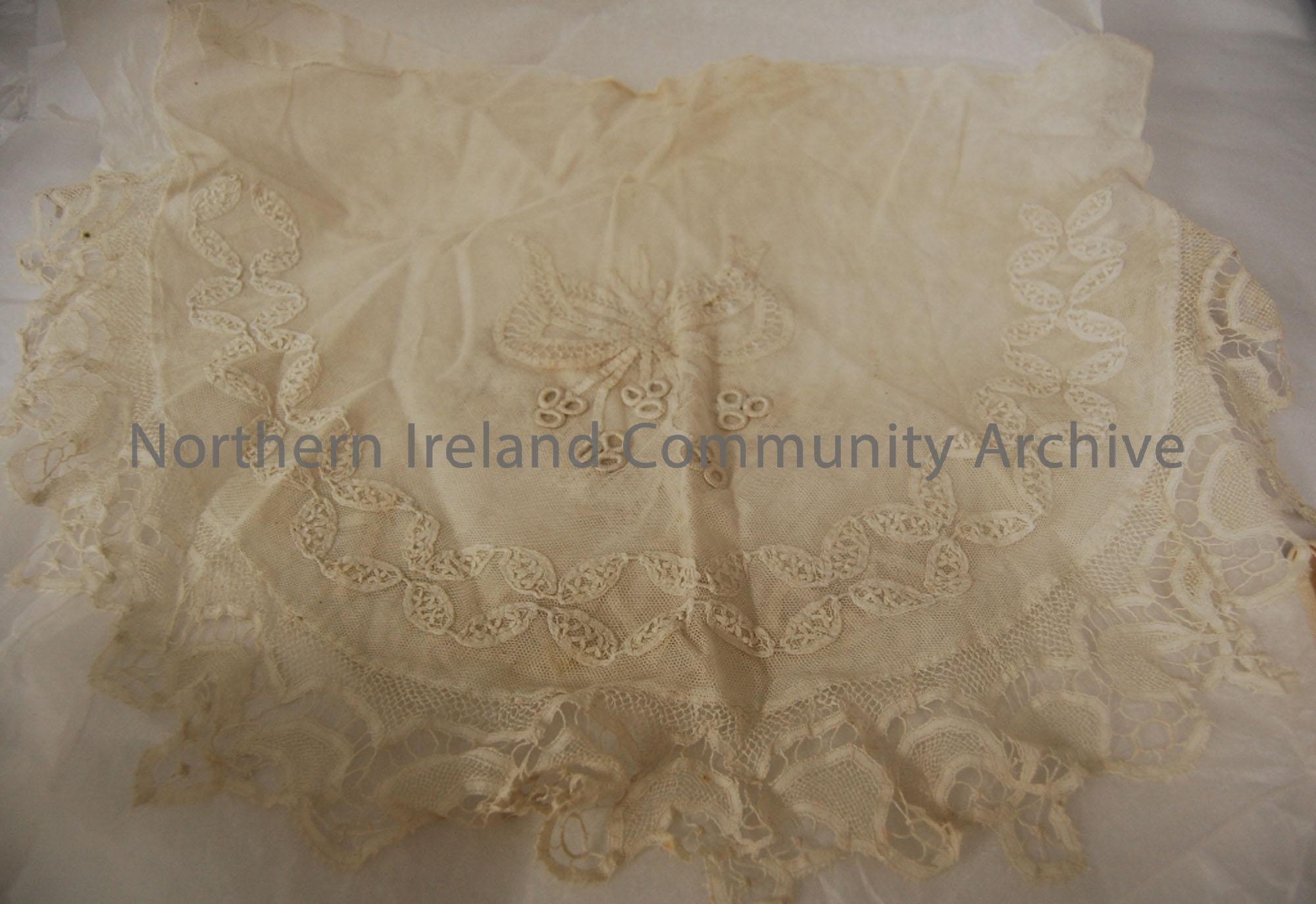 White lacework stiched on both sides with a leaf and bow pattern. It’s a semi circle shape and has frilled edges.
