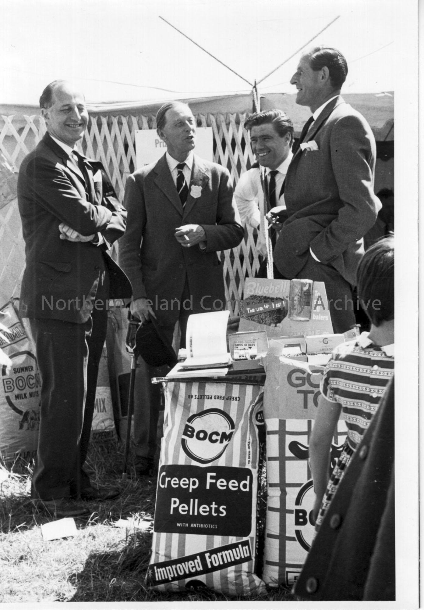 Photographic print of men talking at a Creep Feed Pellets stall.