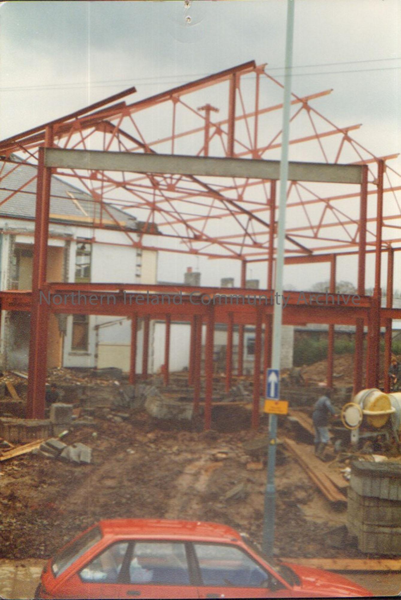 Colour photograph of the building of Riada House Extension. Image of red metal frame of a building with a red car at the bottom..