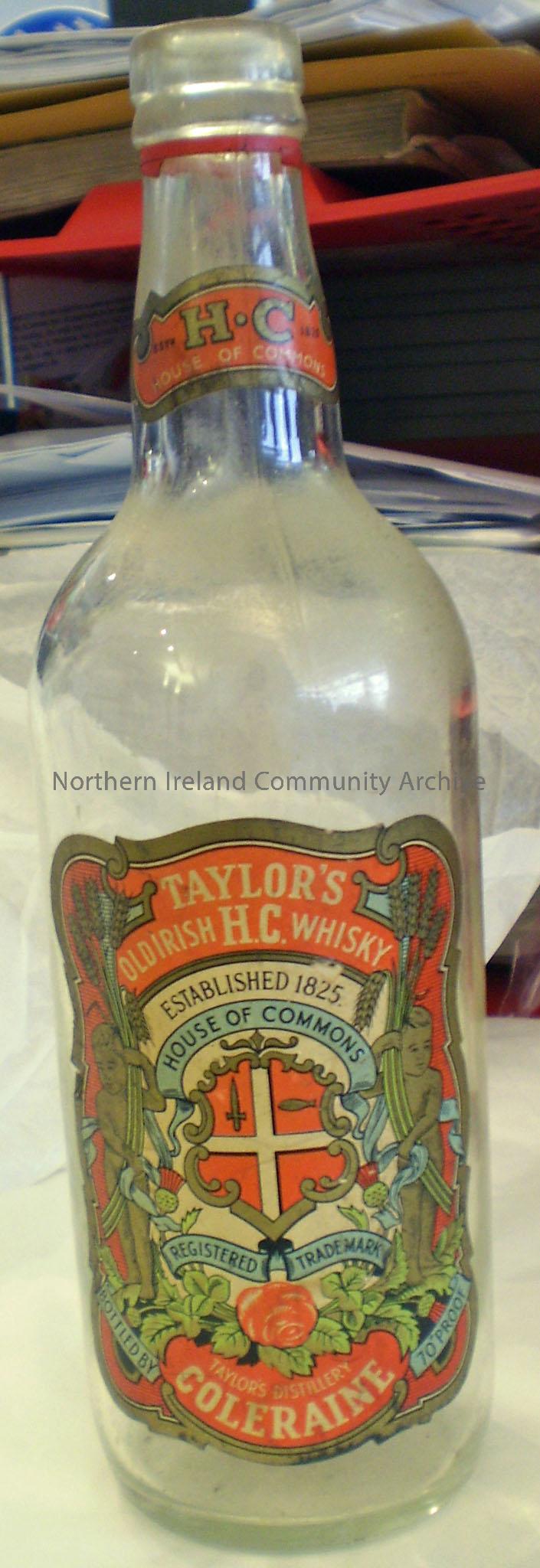 Large, curved, glass Taylor’s Coleraine whisky bottle with decorative label. Label reads ‘Taylor’s Old Irish H.C Whisky, Established 1825, House of Co…