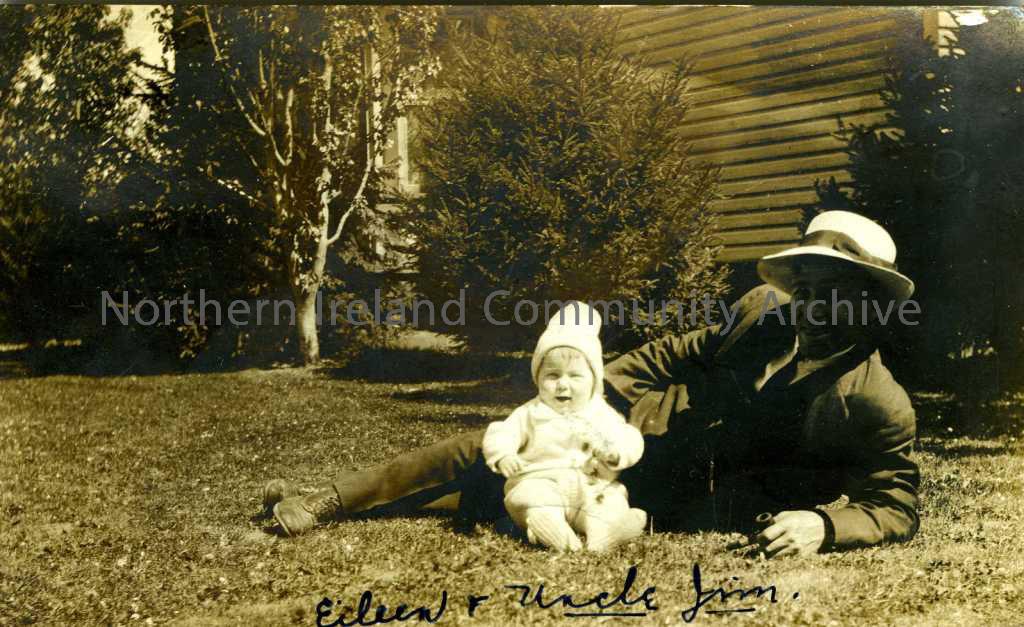 Black and white photographic postcard of a man lying on grass with a baby. Handwritten on the front is ‘Eileen & Uncle Jim’. Sent from Kelowna BC, Can…