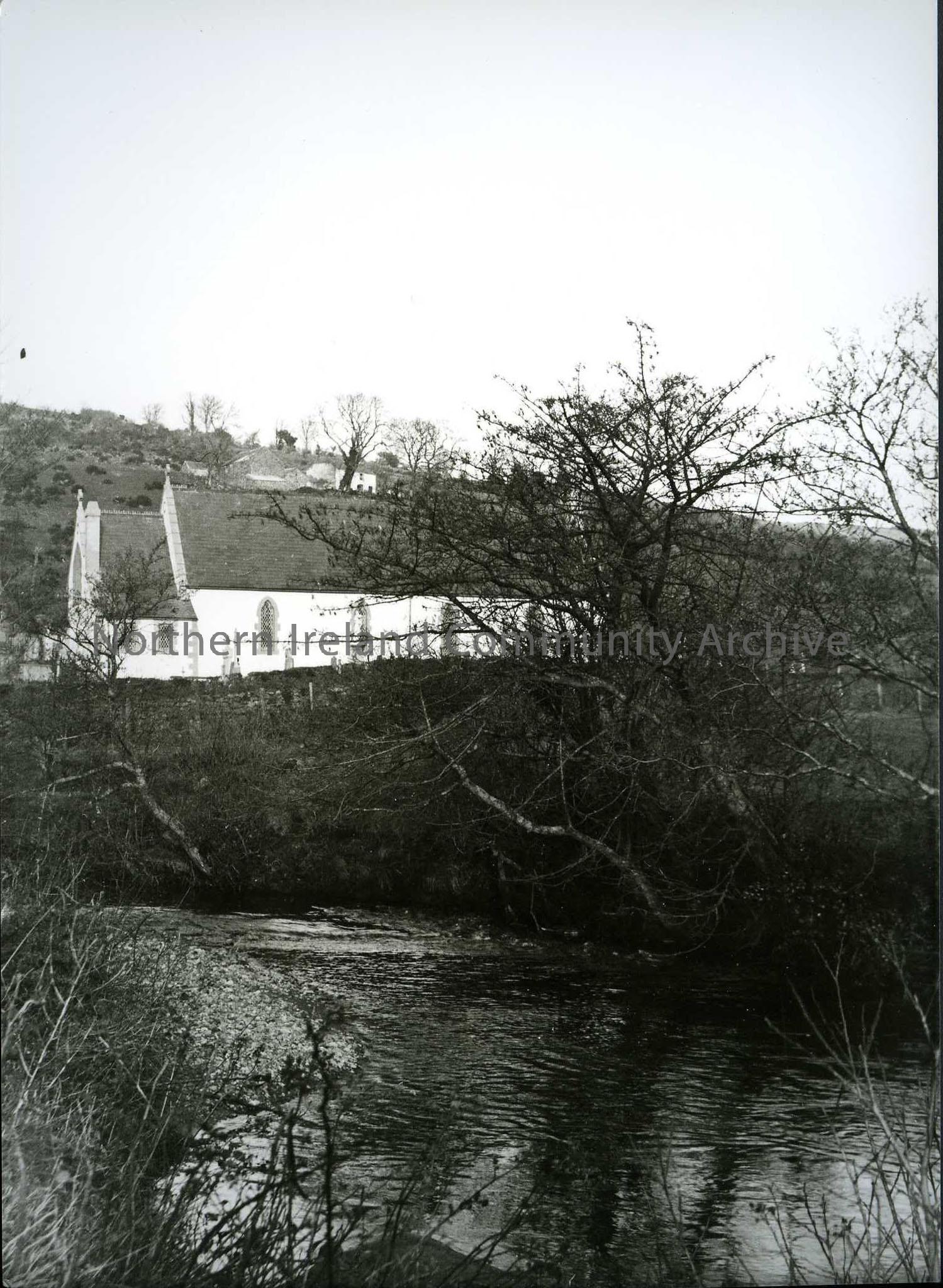 Printed black and white photograph – River and trees in the foreground with a Church behind.
