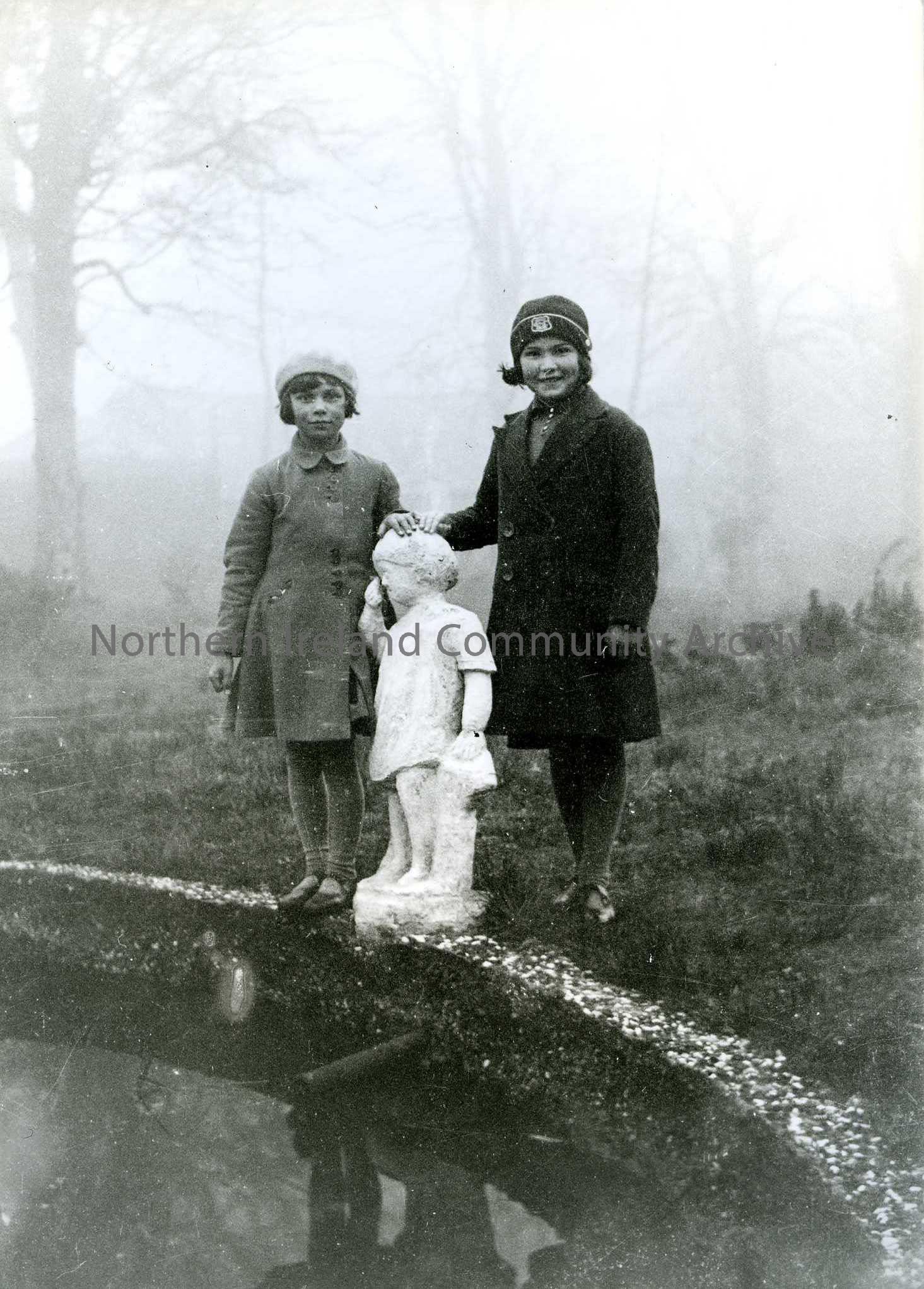 Printed black and white photograph – Olive Craig (nee Henry) standing with another girl beside a garden statue.