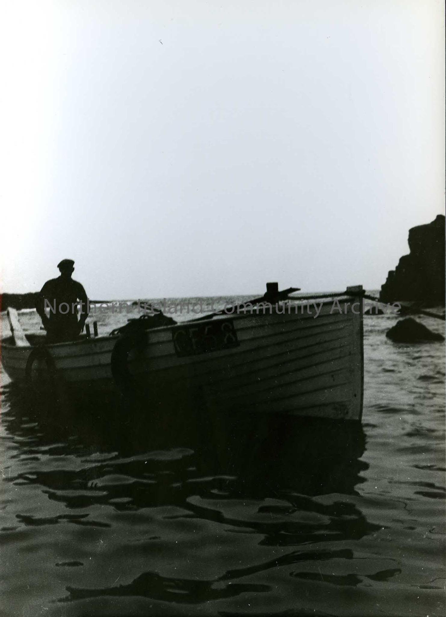 Printed black and white photograph – Man in a boat on water. Painted on the boat is CE58.