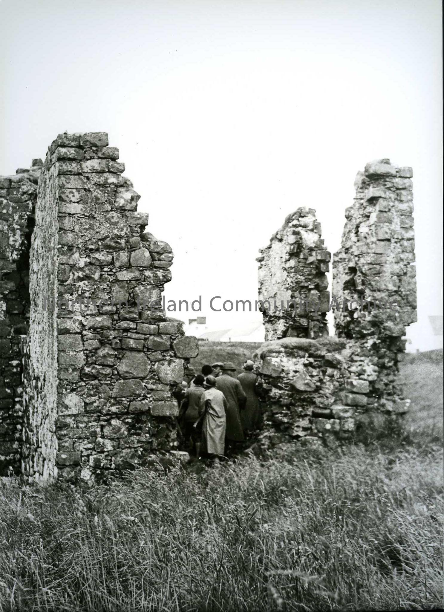 Printed black and white photograph – Group of people (facing away from the camera) at a ruin.