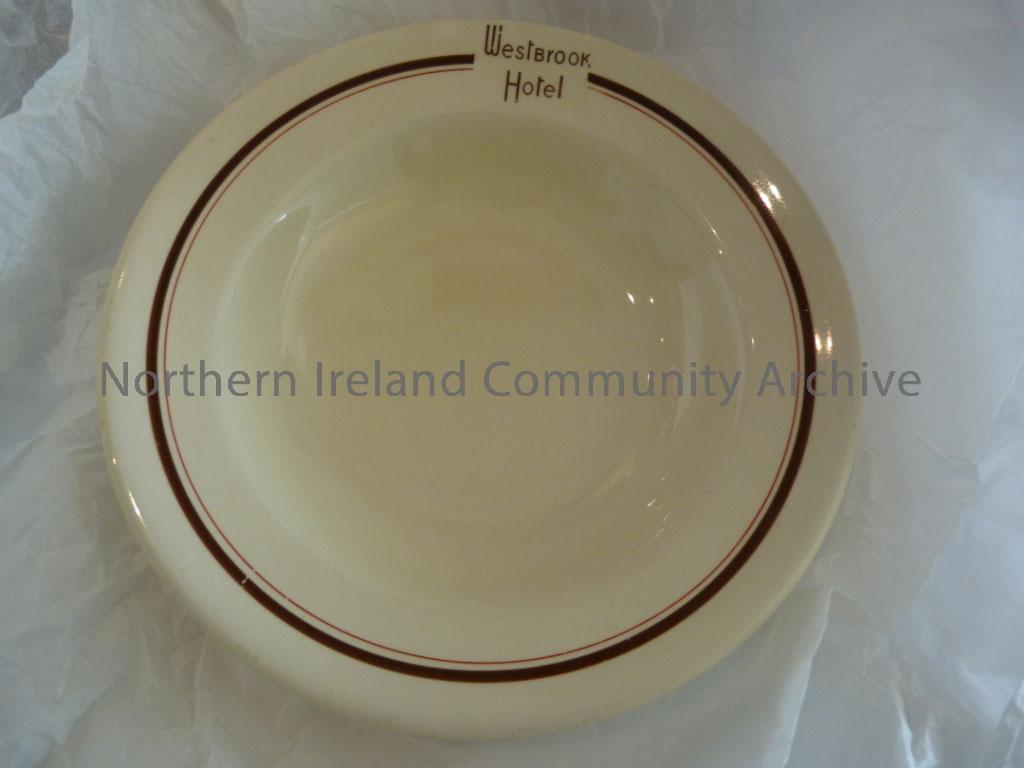 Cream shallow bowl with a brown and red line around it and ‘Westbrook Hotel’. Westbrook Hotel was in Railway Place, Coleraine. Red cross marked on the…