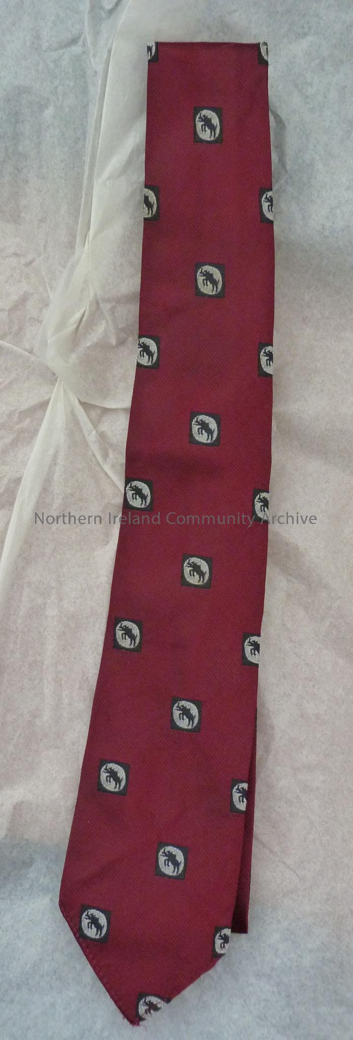 Maroon neck tie with images of a black boar in a white circle inside a black square across it.