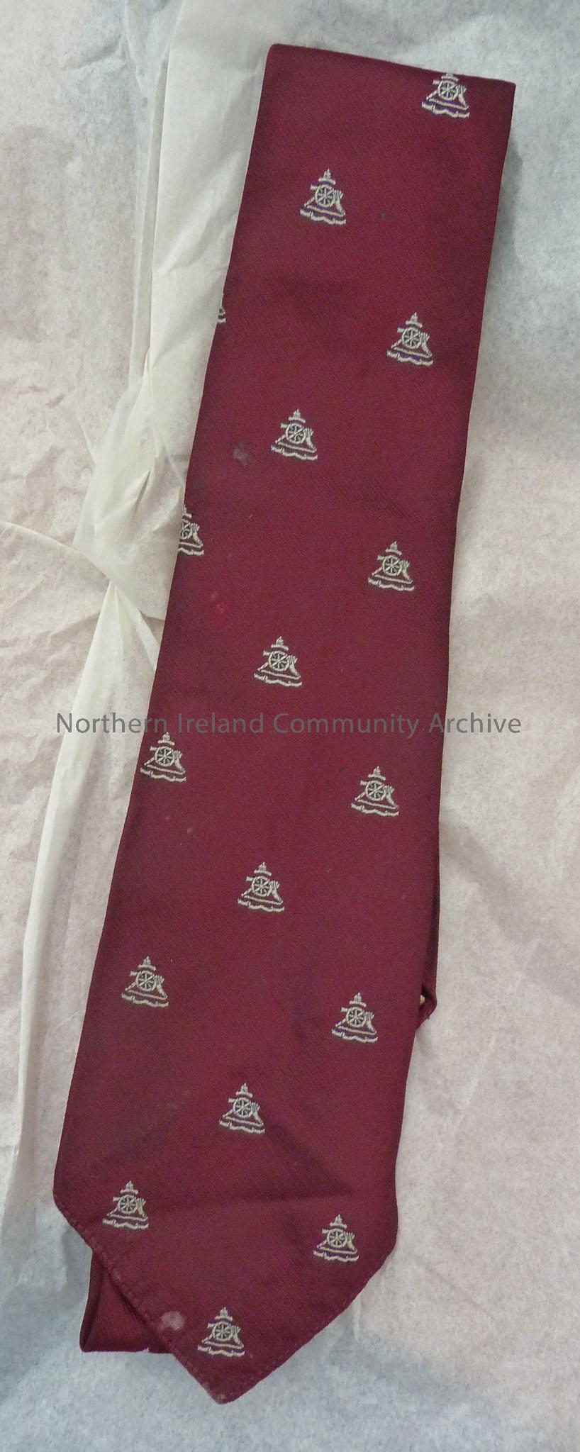 Maroon neck tie with images across it of a canon with a crown above.