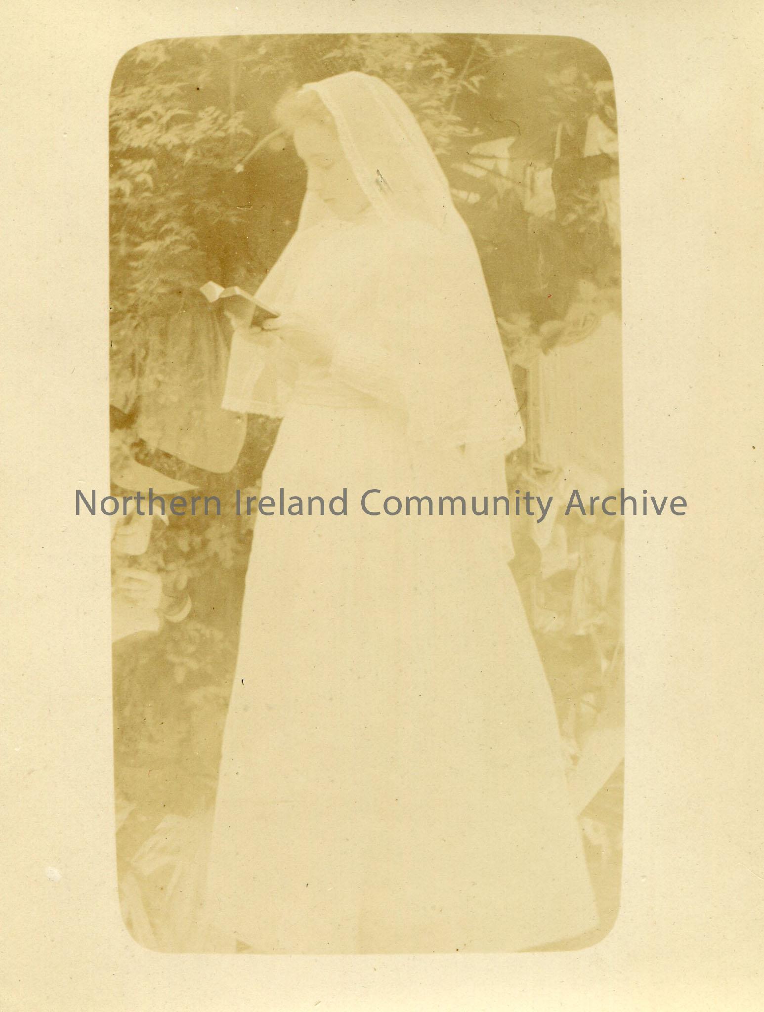 Black and white photograph of a young woman in a white dress and veil looking at an open book.