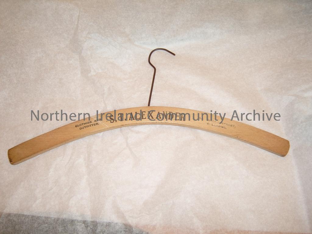 wooden clothes hanger with wire hook. printed onto one side of the hanger is Clothier and Outfitter S.T.Alexander, 10 Bridge Street, Coleraine. This drapers shop was open in the 1930s and 1940s (4645)