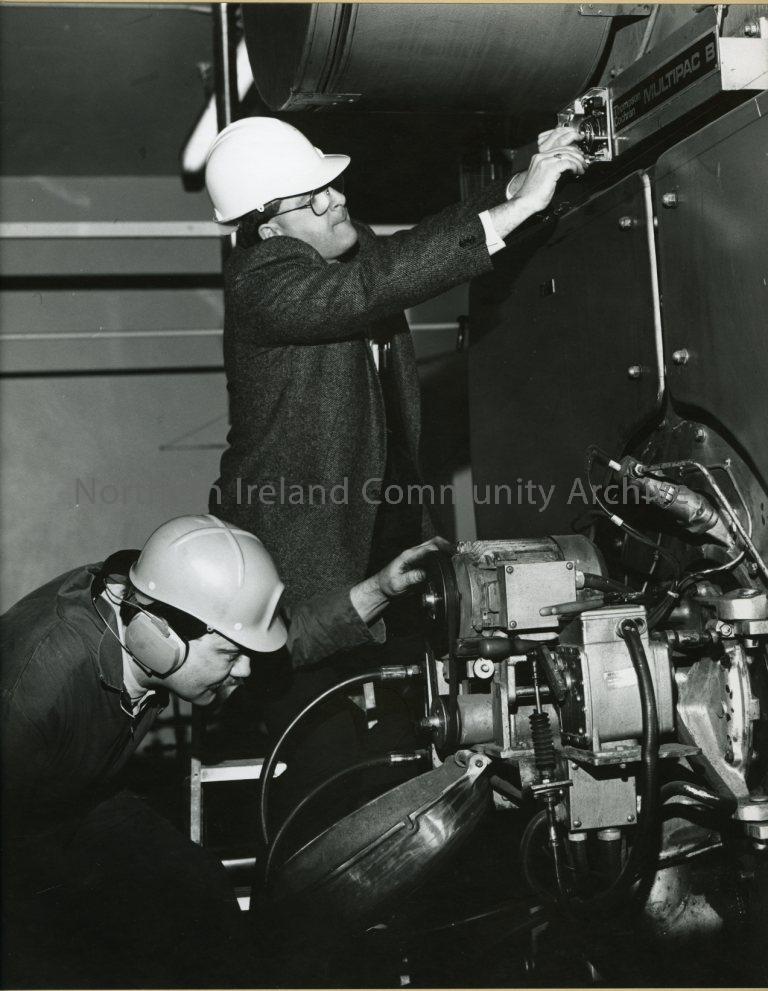black and white photograph of 2 men working with a piece of machinery wearing hard hats (3733)
