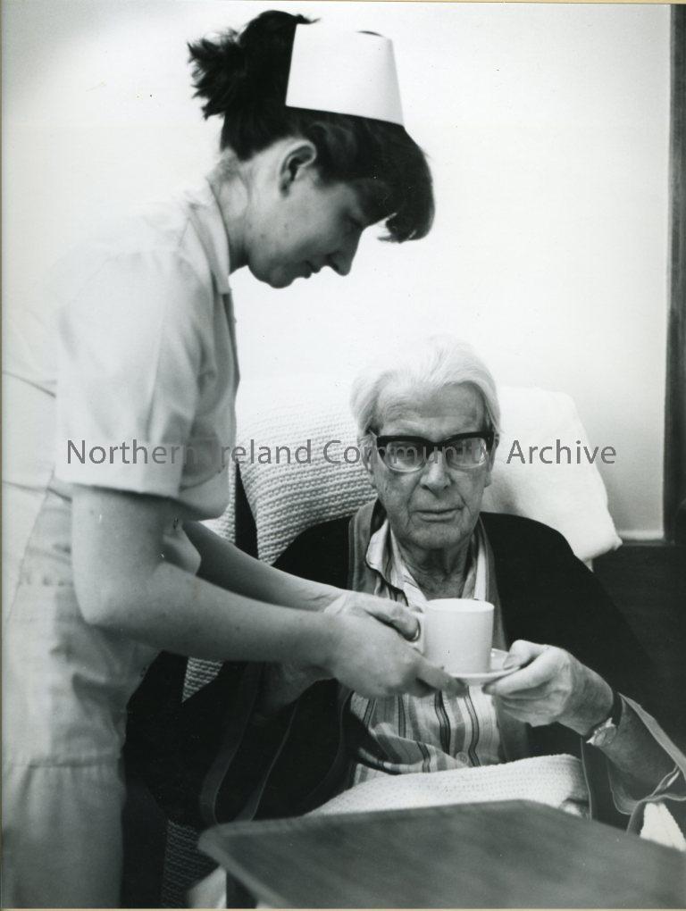 black and white photograph of a nurse giving an elderly man a cup of tea/coffee (6707)