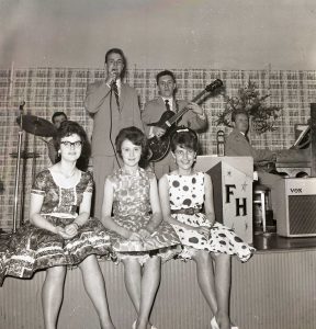 A showband plays as 3 ladies are sitting in a row on the stage