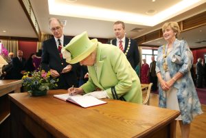 Photograph of Queen Elizabeth II signing the visitor book at Royal Portrush Golf Club.